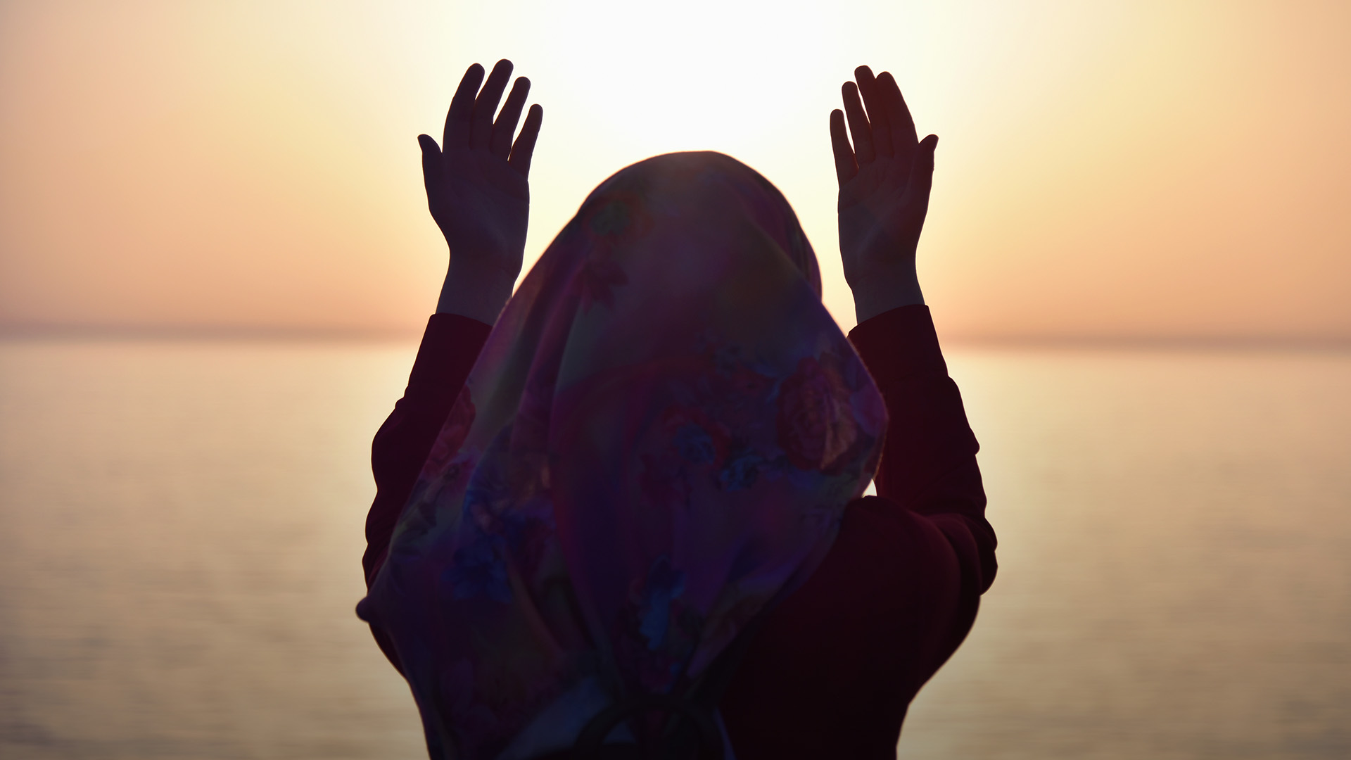 Muslim woman praying in the ship praying at sunset with hands up.